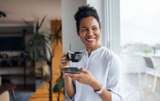 woman sipping coffee by window smiling with teeth