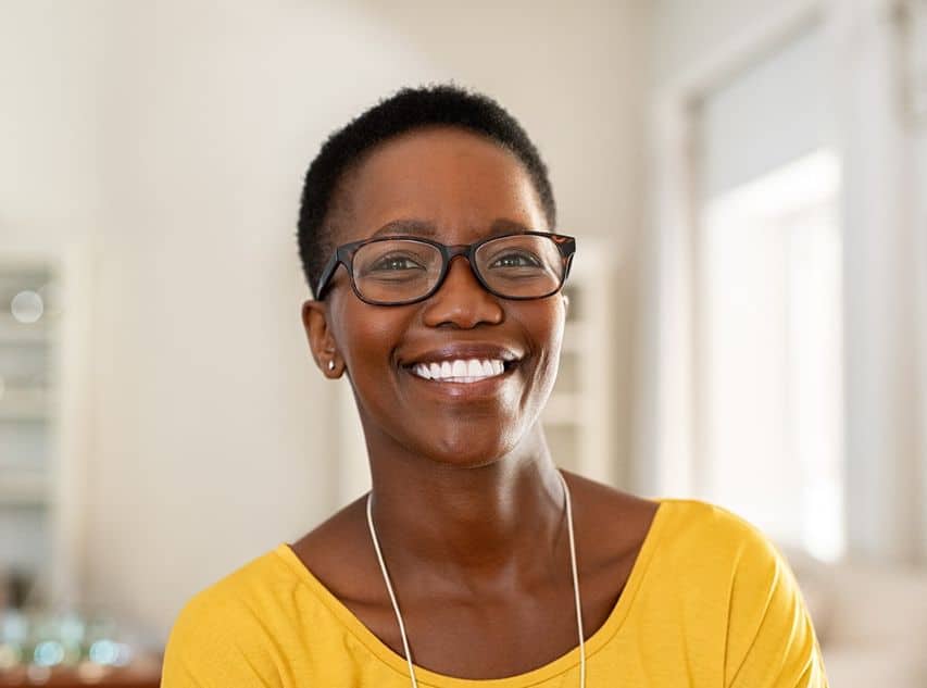 Updated Smile Makeover content image 1 A woman with short hair and glasses wearing a yellow shirt and smiling